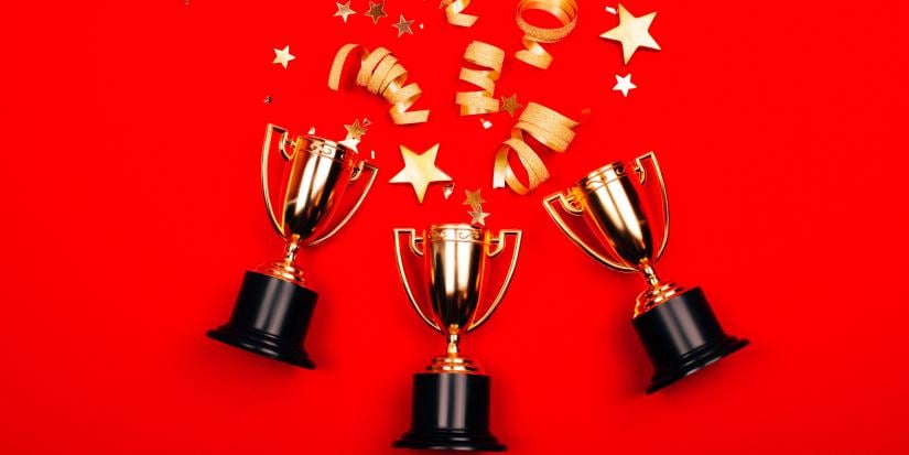 Three golden winner cups with confetti on a red background.