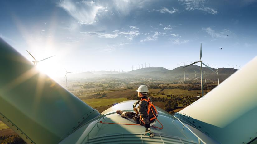 Technician sitting atop a large wind turbine in a wind farm
