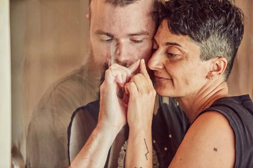 Two people seperated by a clear screen touch faces and hands together