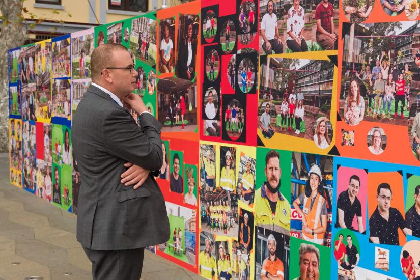 A man in a suit looks at a wall of photographs installed as a mural on a Parramatta street.