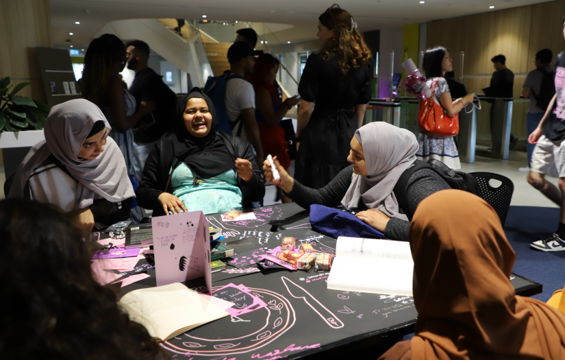 Students laughing and sitting at a table covered in drawings and paper