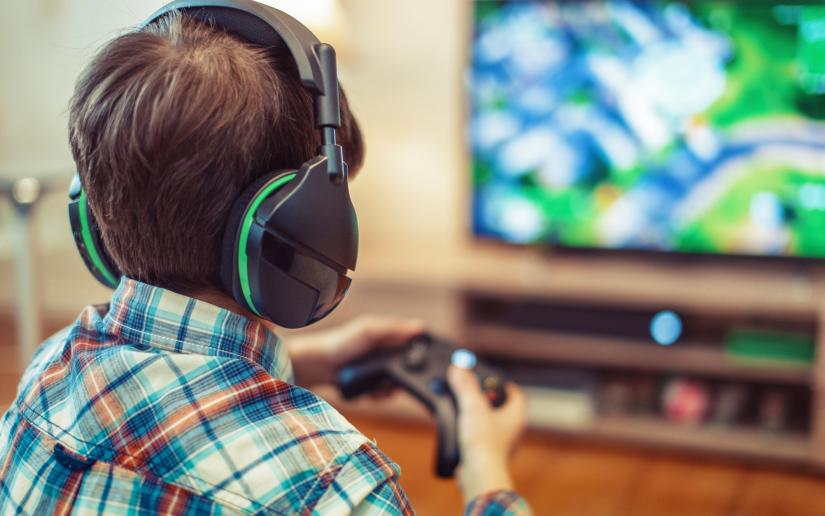 A child wears headphones and holds a remote controller to play video games.