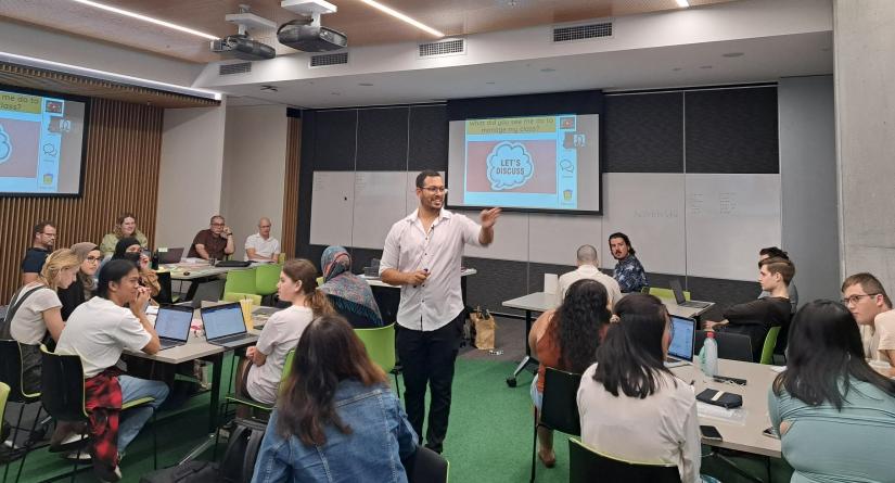 inside a classroom, a class of UTS students are seated with one man standing amongst them and speaking to them