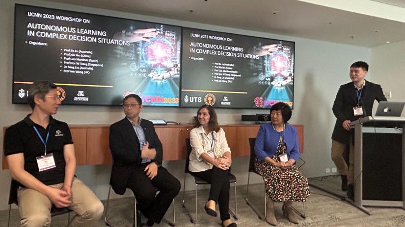 Seated on a panel, from left to right, Prof. Xin Yao, Prof Xue Li, Prof Marley Vellasco, Prof Jie Lu. Dr Feng Liu is standing beside a podium.
