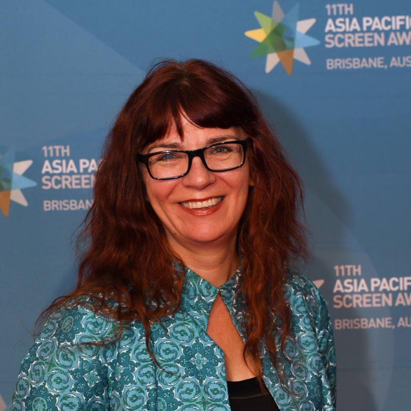 Melanie Coombs smiles at the camera in front of a blue media wall