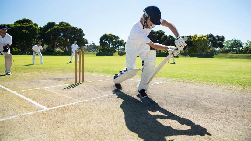 Cricket player in whites demonstrating a cricket stance blocking at a park