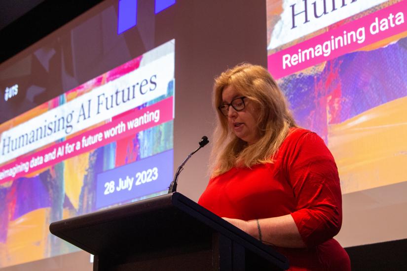 A woman wearing a red dress speaks at a lecturn, reading from notes