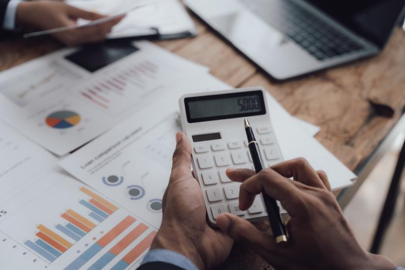 an individual uses a calculator, documents with graphs in the background