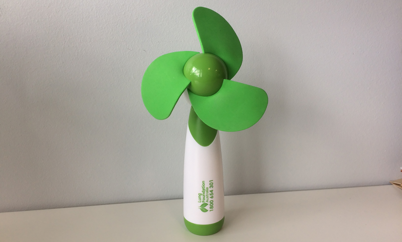 Hand-held fan with white handle and bright green blades. Text on fan reads, 'Lung Foundation Australia' next to a Lung Foundation Australia logo which is a pair of lungs in green that resemble leaves