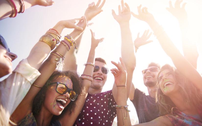A group of people gathered at a festival with their hands in the air and looking excitedly in the distance.