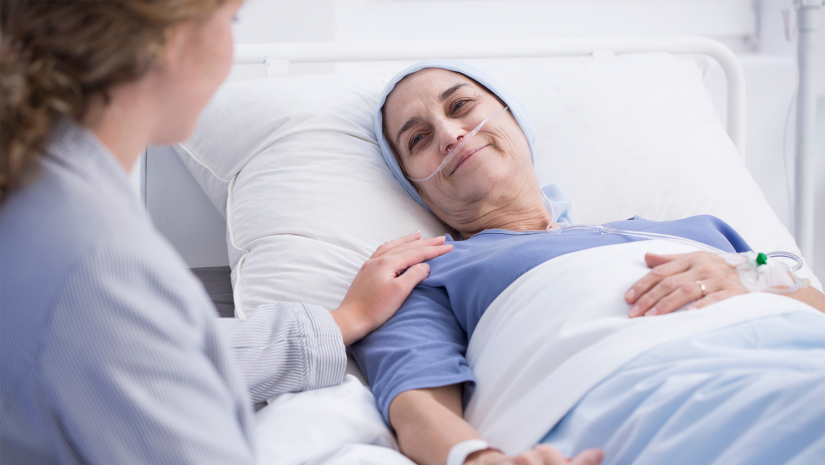 Senior woman with head scarf smiles at carer from hospital bed
