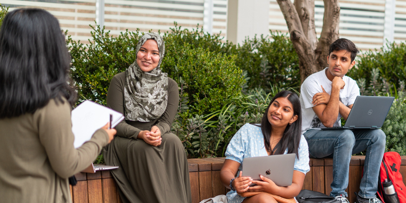 A group of students sitting down, listening to a person in the foreground