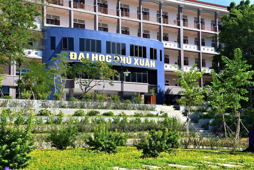 The entrance to Phu Xuan University, green garden in front of a blue and pink office building