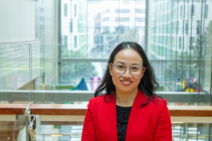 Tien wears a red blazer and smiles for the camera in Building 10