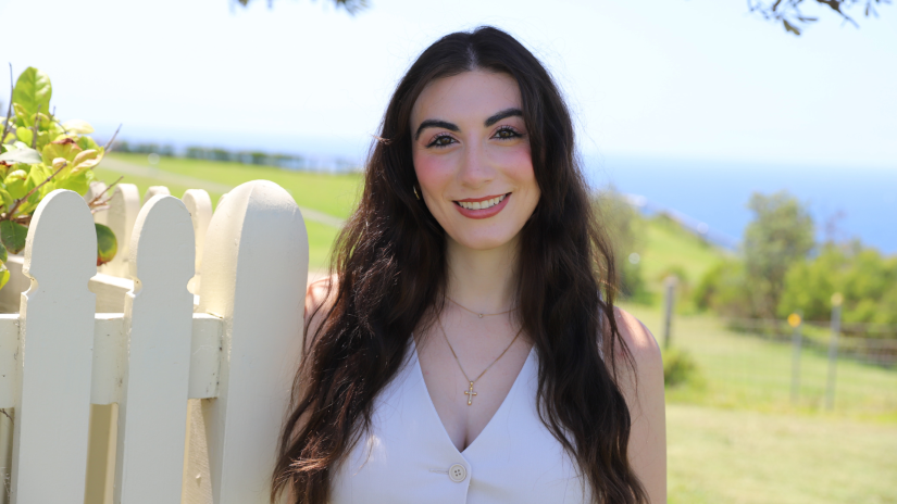 Katherine Turk standing outside next to a fence, smiling with blue sky behind.
