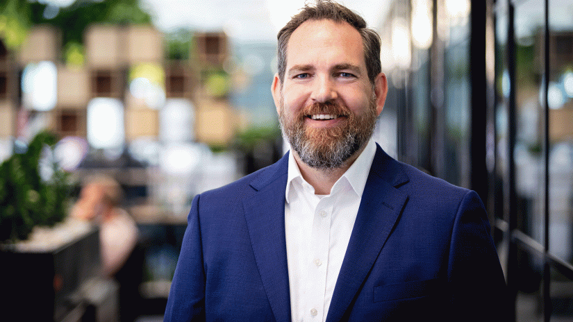 Male academic in blue suit jacket and white shirt smiles directly at camera in an office setting