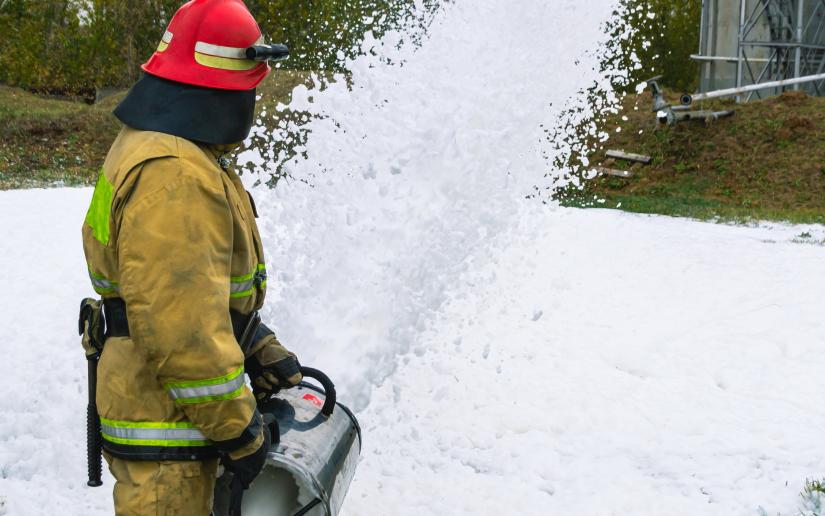 Stock picture of a firefighter in protective clothing extinguishing a fire by feeding foam.