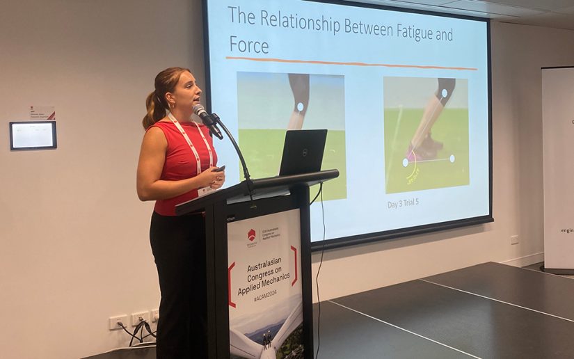 Zoe cross stands at the podium to present her work to an audience at ACAM 2024