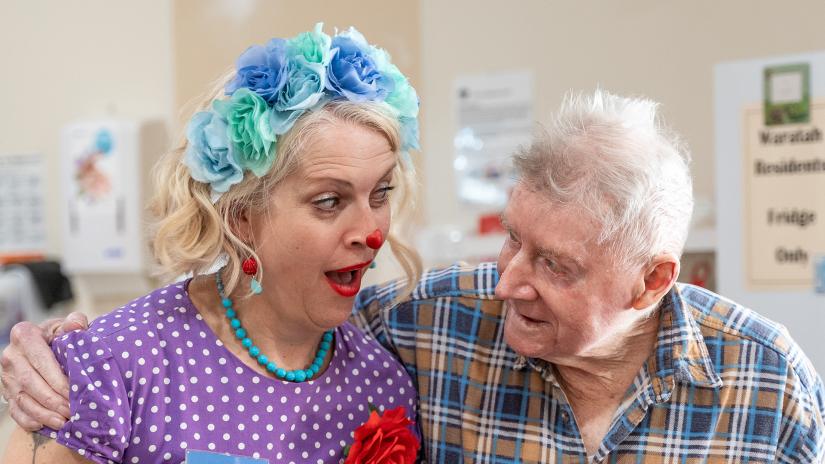Laughter care clown and elderly man are looking at each other and smiling.