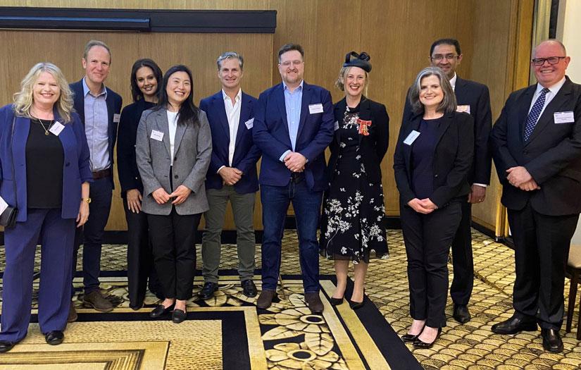 Group of UTS alumni in business attire smiling and looking at the camera