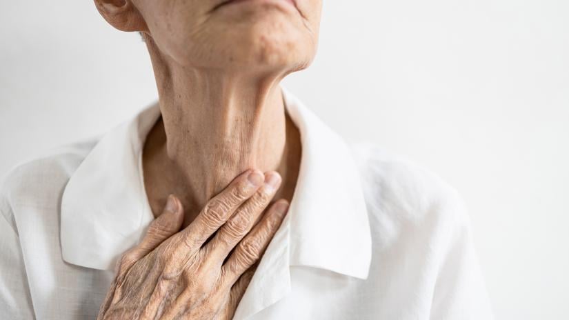 Elderly person with their hand delicately touching their throat