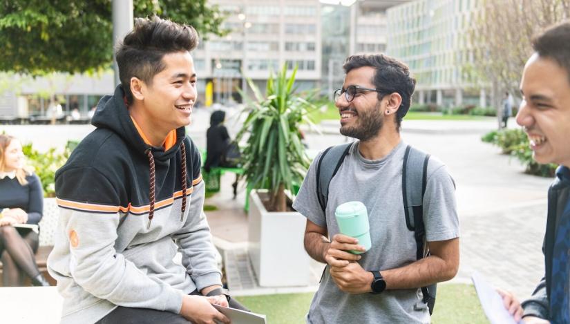 2 young male students are talking. One is holding a coffee