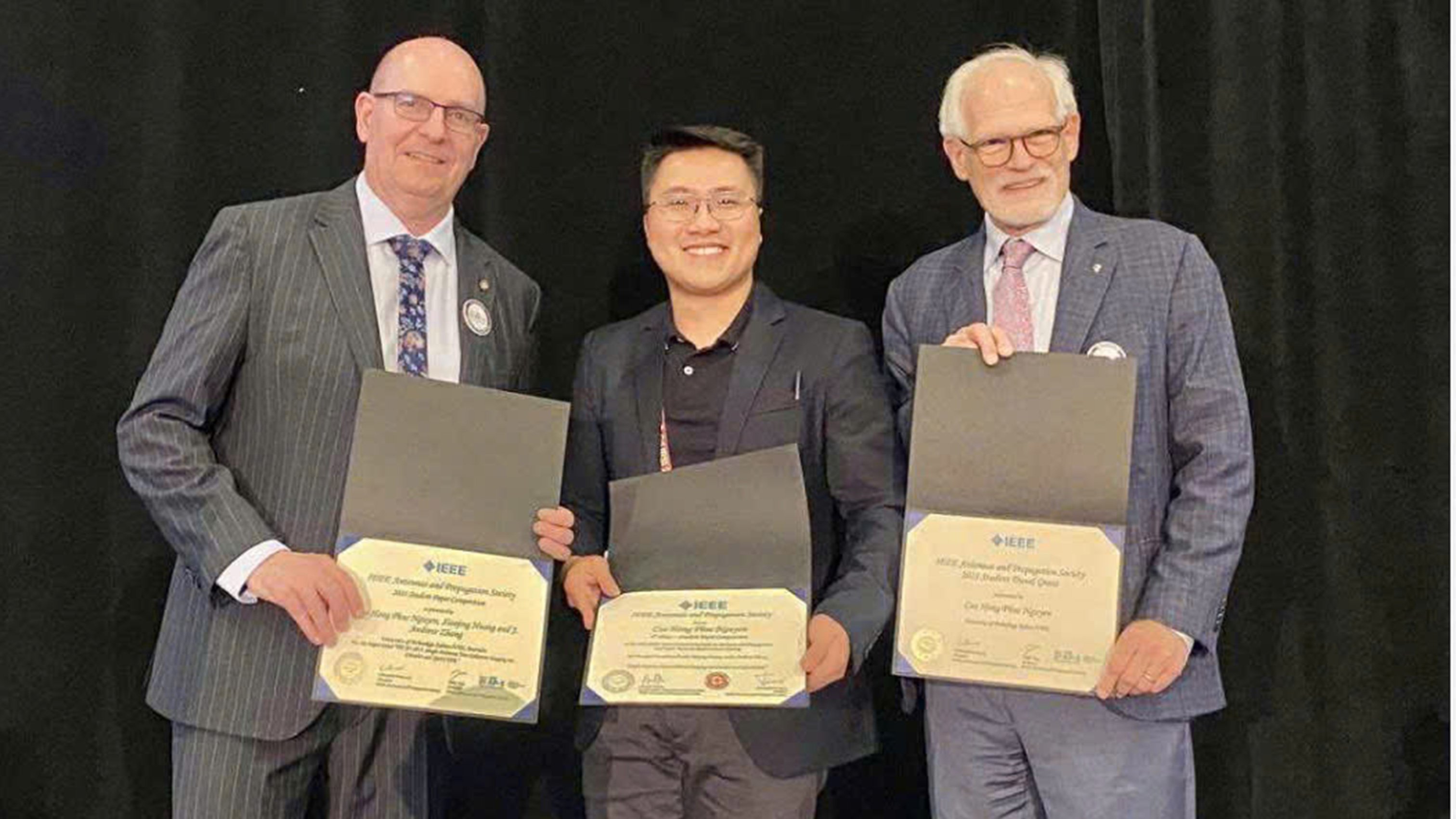 Three people stand holding awards