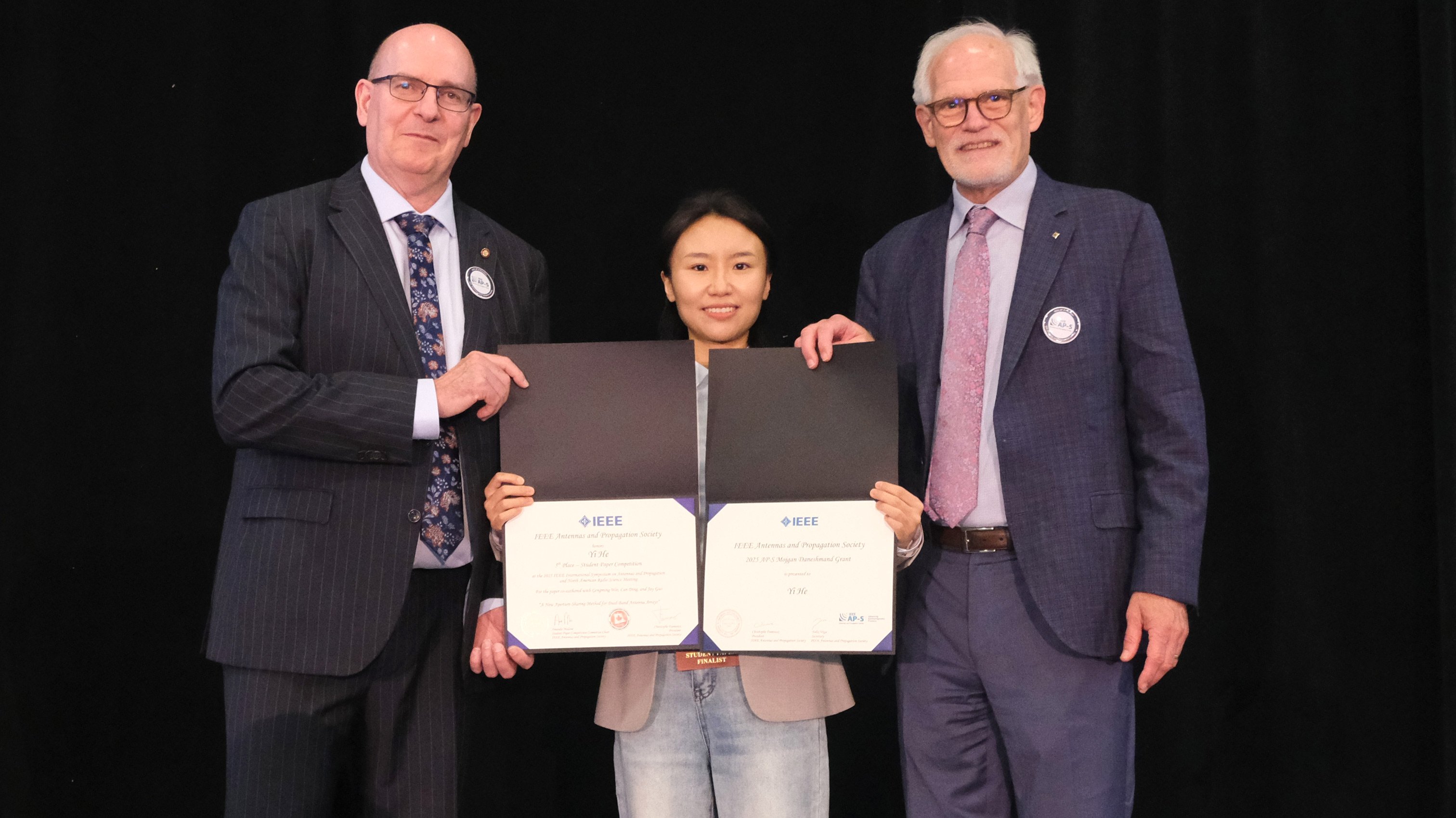 Two people stand aside Yi He with two awards