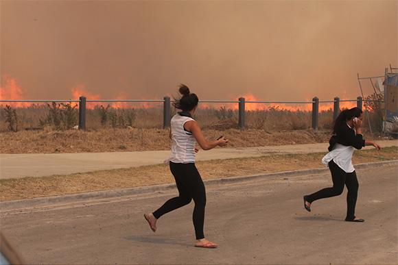 Two women running across a road to escape a bush fire