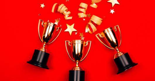 Three golden winner cups with confetti on a red background.