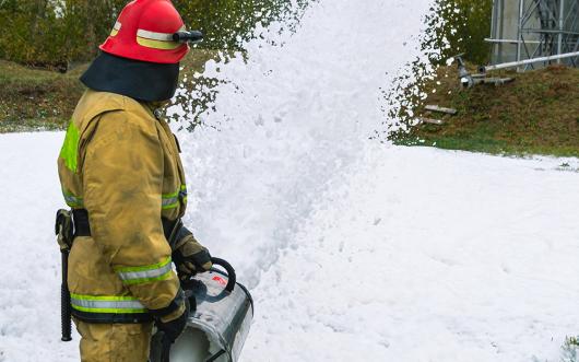 Stock picture of a firefighter in protective clothing extinguishing a fire by feeding foam.