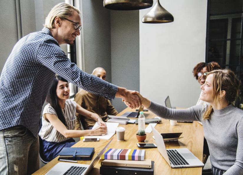 Students sitting around a table with a supervisor shaking the hand of one of the students.