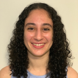 A headshot of Samantha Morris from the shoulders up. Samantha has shoulder-length curly black hair and is wearing a light blue tank top. The background is plain.