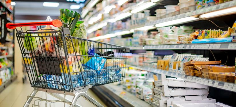 A shopping trolley filled with groceries in a supermarket aisle