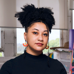 Claudia looks at the camera, with black hair tied back and orange earrings