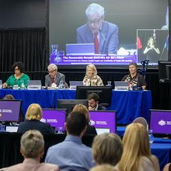 Large screen shows man speaking in front of seated crowds at The Royal Commission into Violence, Abuse, Neglect and Exploitation of People with Disability