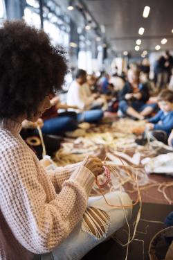 Woman working on craft project close up, art fair visible in the background.