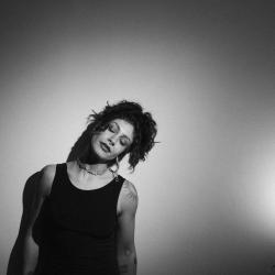 black and white publicity image of woman in black singlet top with curly dark hair