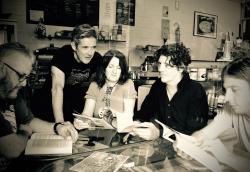 black and white image of five people sitting around a table talking and looking at books