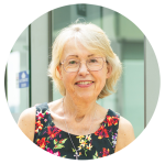 Imelda Gilmore has short blonde hair and is wearing sleeveless top that is black with a flora print. She wears glasses and is smiling at the camera.