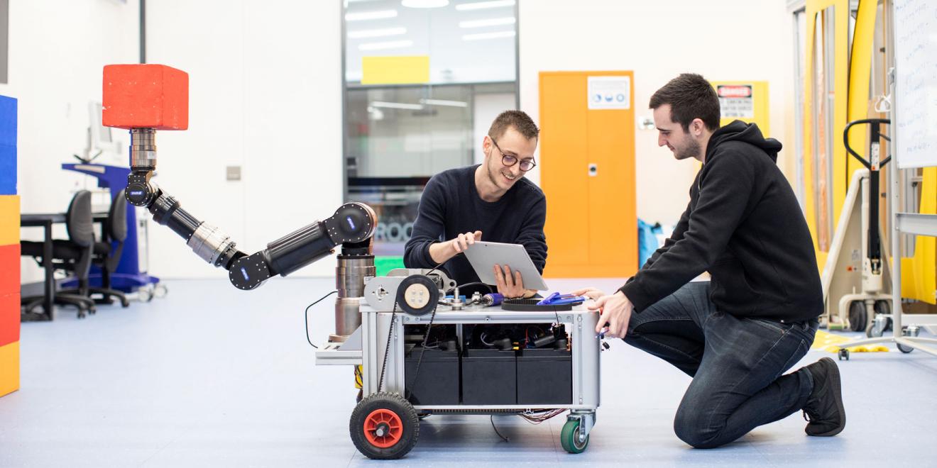 Two men crouch with a piece of robotic equipment they are testing