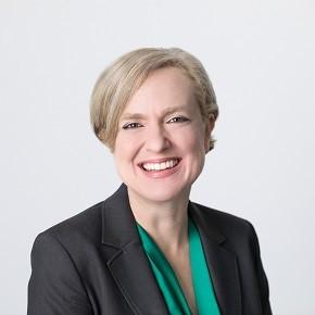 professional image of woman with short blond hair smiling at the camera. she is wearing a green shirt and grey blazer.