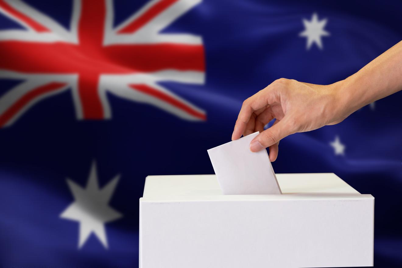 a hand putting a ballot in the ballot box with Australian flag in background