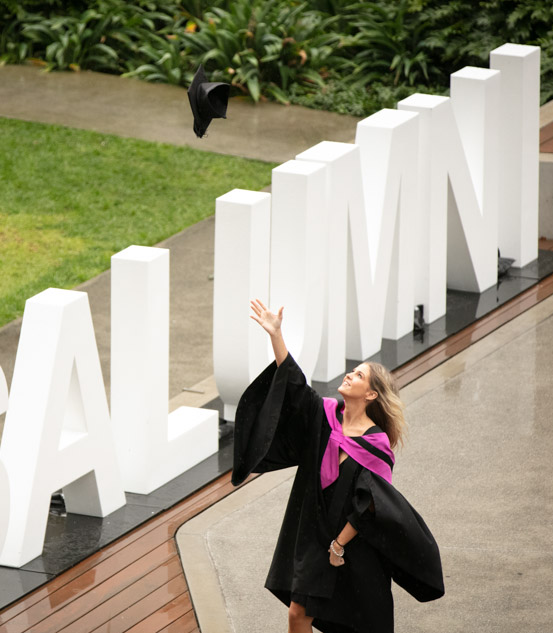 Student throwing grad cap in front of alumni letters