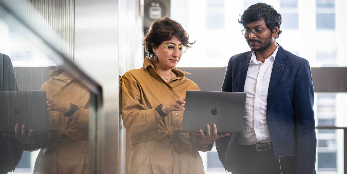 Man and woman in an office corridor looking at a laptop screen