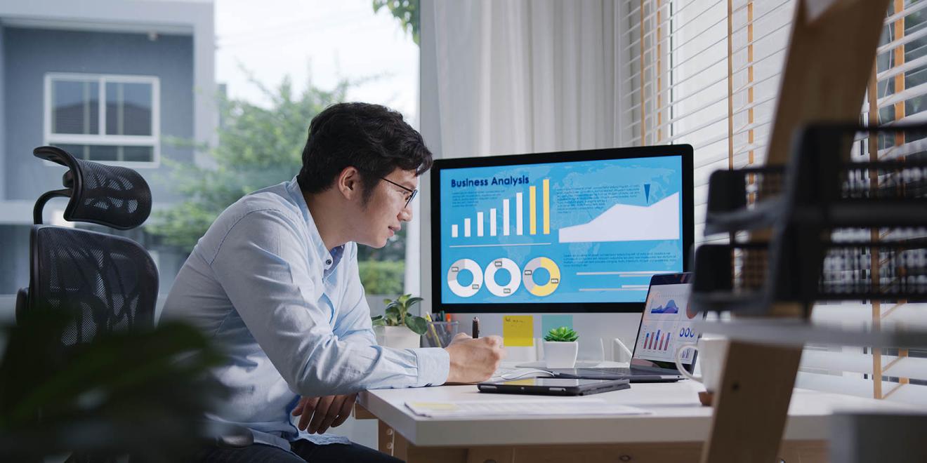 Person sitting at desk looking at multiple computer monitors with data analytics graphics on the screen