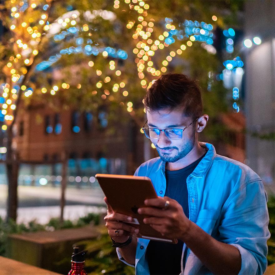 International student looking at iPad at night in Darling Square, Sydney