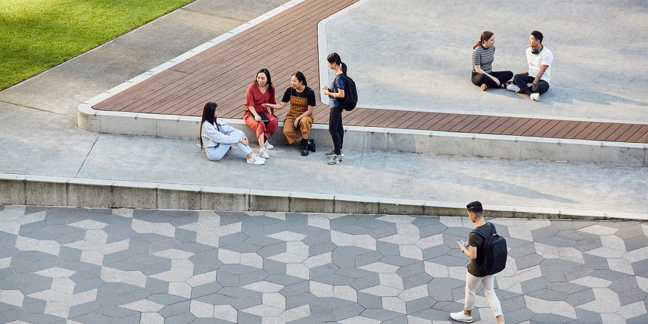 Groups of students sitting next to a green area on a university campus