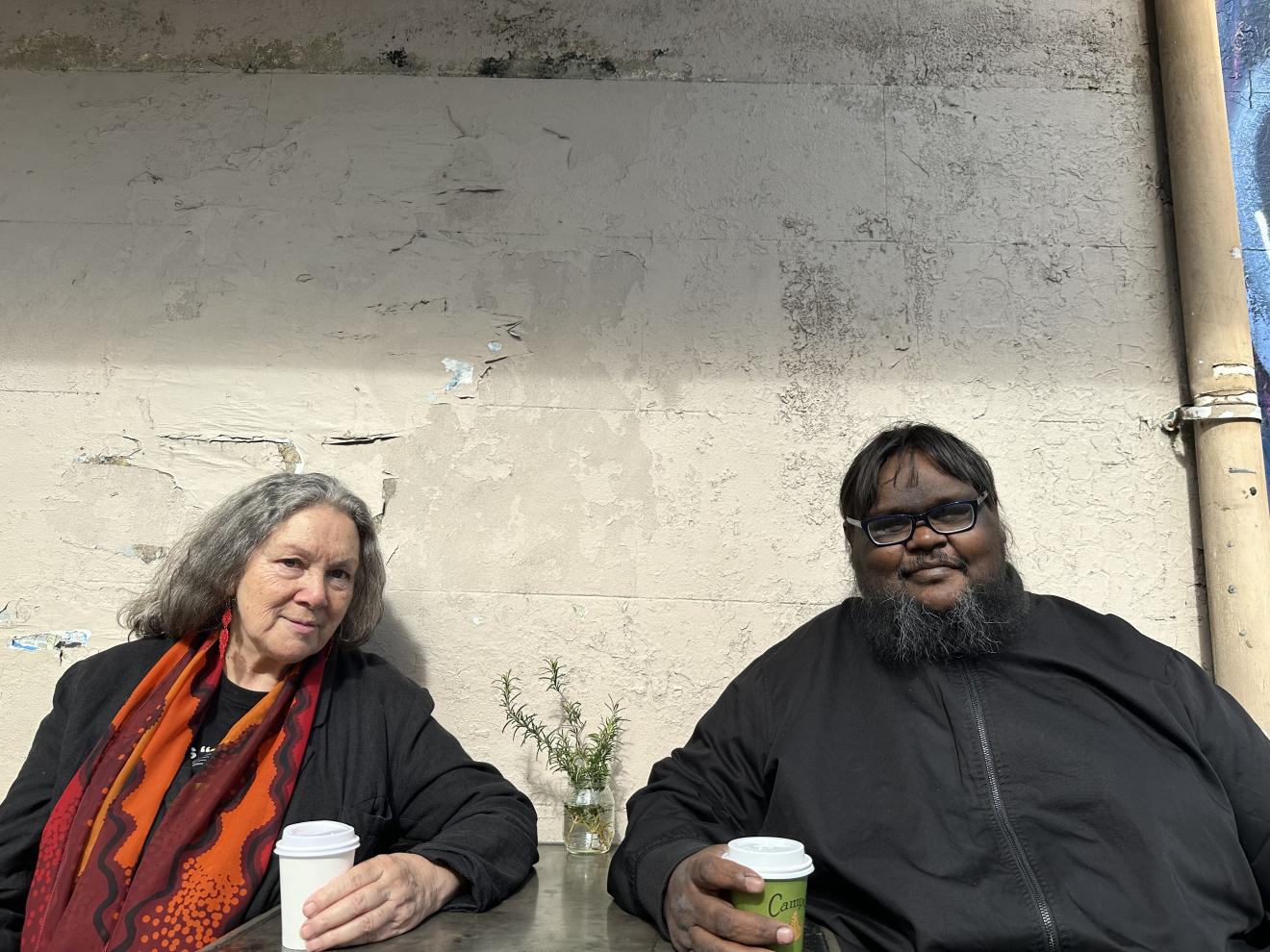 two aboriginal people sitting at a table drinking coffee outside a community education centre