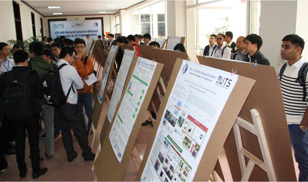 People walk around and study a display of posters on frames running down the centre of a long room.